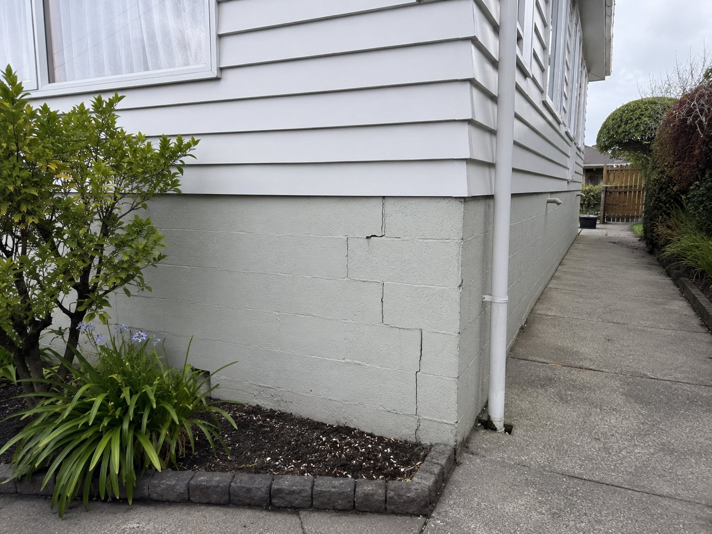 Stepped crack through the painted block (masonry) foundation at the corner of the house